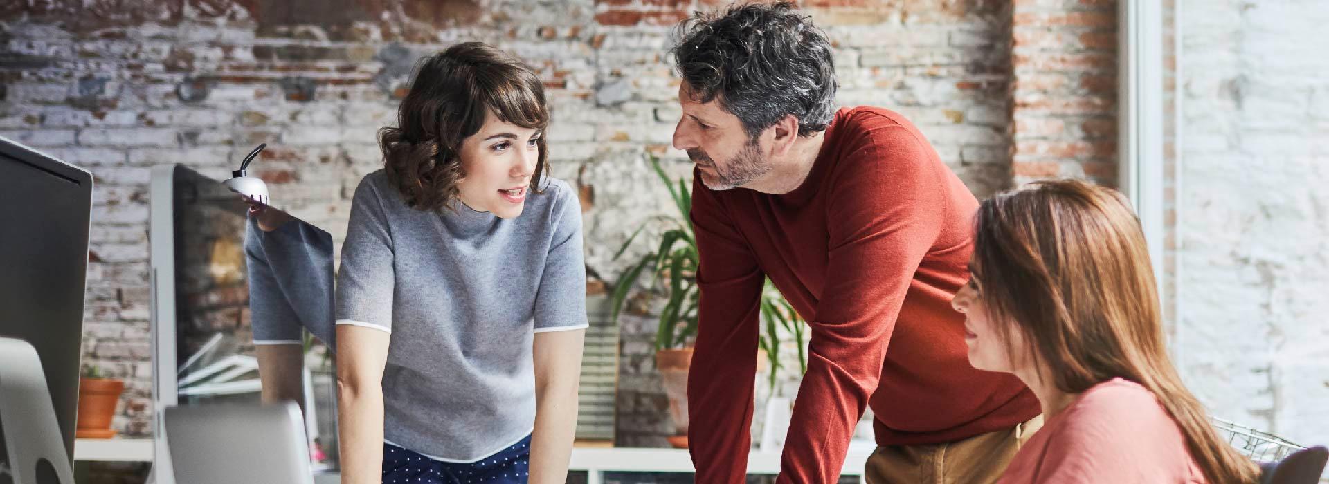 three people talking in an open office next to computers