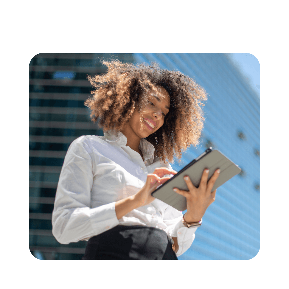 Woman with curly hair wearing white shirt holding tablet outdoors against blue sky and building